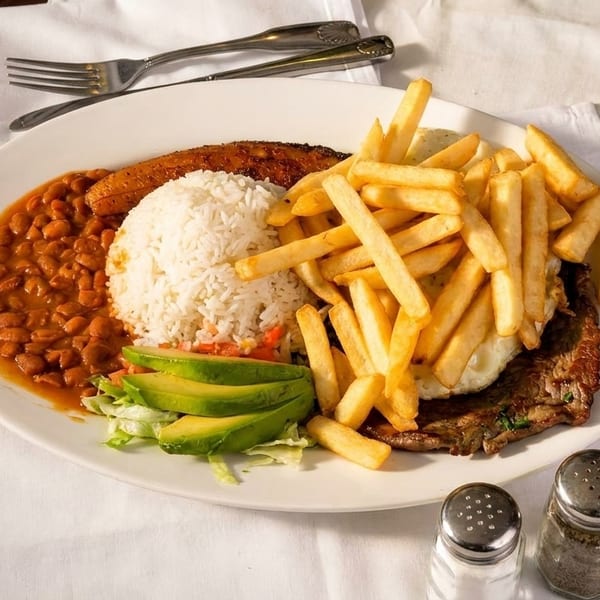 A large plate of steak, french fries, rice, beans, plantain, and avocado slices.